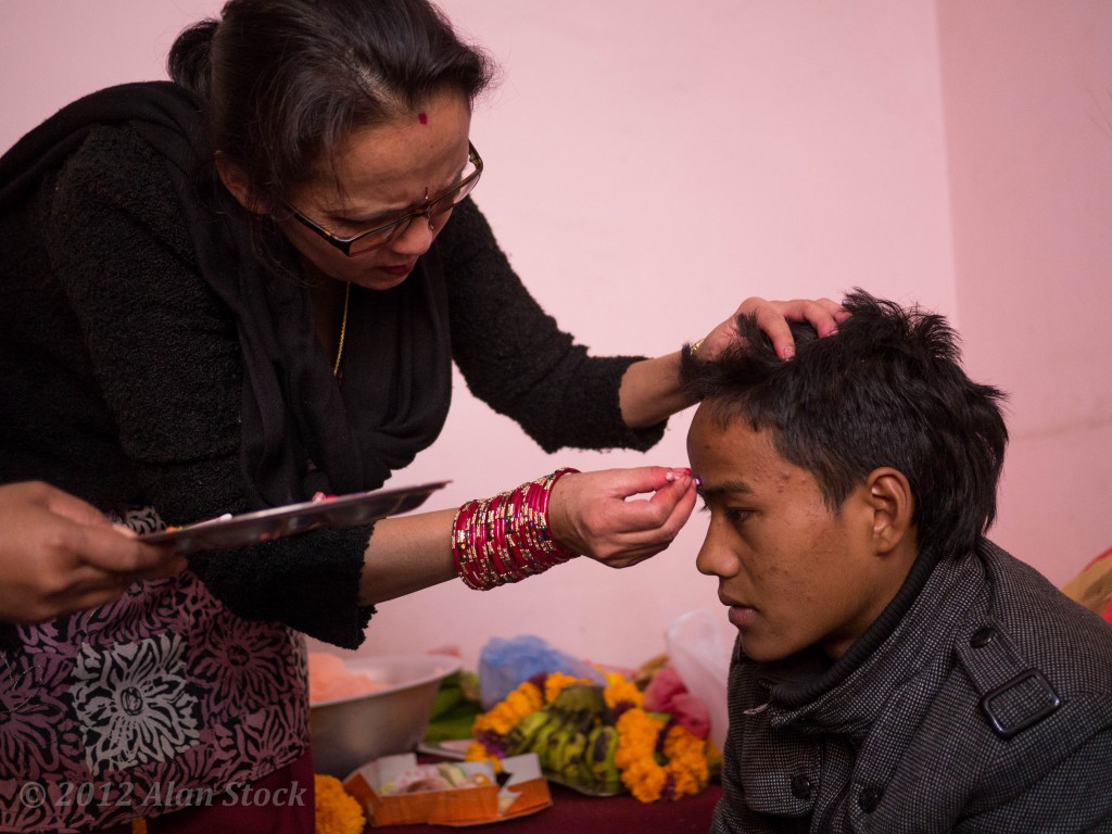 The aunt carefully dots the tikka line on her son's forehead.